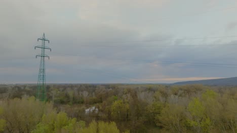 Luftaufnahme-Eines-Grünen-Hochspannungsmastes-Im-Wald-Vor-Blauem-Himmel