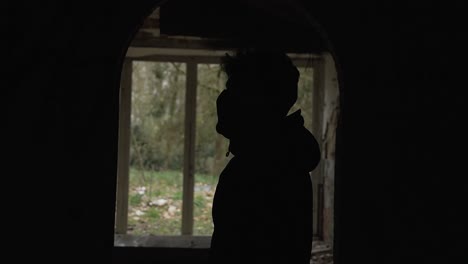 Silhouette-Eines-Jungen-Mannes-Mit-Schwarzem-Kapuzenpullover-Steht-Im-Flur-Und-Vor-Einem-Großen-Fenster-In-Einem-Verlassenen-Herrenhaus