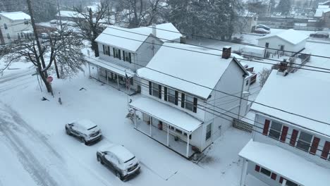 Verschneite-Straße-Mit-Weißen-Häusern,-Roten-Akzenten,-Autos-Und-Kahlen-Bäumen
