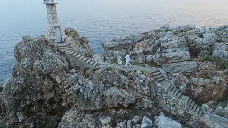 Kalamota-Island,-Adriatic-Sea,-Croatia---A-Couple-Heading-Towards-the-Lighthouse-to-Appreciate-the-Sunset---Aerial-Pullback-Shot