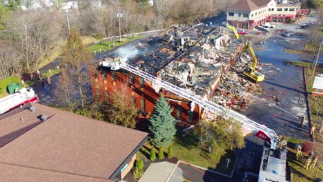 Mutige-Feuerwehrleute-Auf-Der-Aufzugsleiter-Spritzen-Wasser-Auf-Die-Decke-Eines-Lagerhauses,-Das-Feuer-Gefangen-Hat