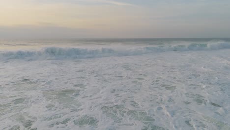 Drone-view-on-ocean-waves-crushing-and-making-foam-at-sunset