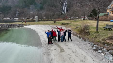 Grupo-De-Turistas-Alegres-Agitando-Las-Manos-Y-Sonriendo-A-La-Cámara-En-La-Playa-Frente-Al-Mar