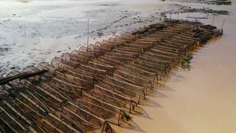 Fish-traps-stored,-waiting-for-the-rains-to-return-on-the-Tonle-Sap-shore-line,-Asias-biggest-inland-lake,-Aerial-drone-fly-over