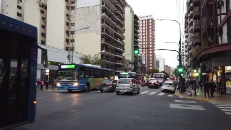 Bulliciosa-Avenida-De-Autobuses-Intersección-Tráfico-Buenos-Aires-Arquitectura-De-La-Ciudad-Puesta-De-Sol-Horizonte-En-El-Barrio-De-Flores,-Edificios-Del-Centro