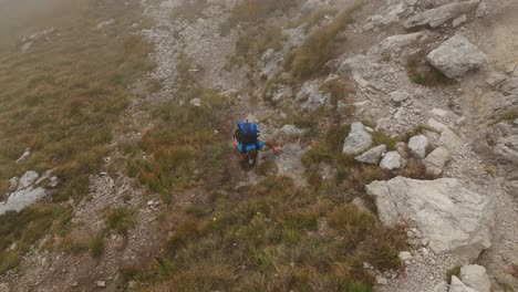 Luftaufnahme-Aus-Der-Vogelperspektive-Eines-Wanderers,-Der-In-Den-Lecco-Alpen-Einen-Berghang-Erklimmt,-Mit-Nebliger-Luft-Im-Hintergrund