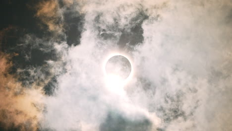 Solar-Eclipse-April-2024-with-clouds-passing-over-the-sun-and-moon-in-the-sky,-epic-cinematic-shot