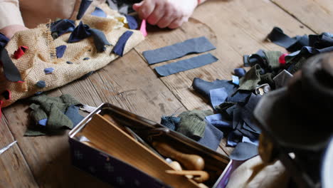 Close-up-of-hand-working-with-textile-pieces-on-a-wooden-table,-alongside-sewing-tools