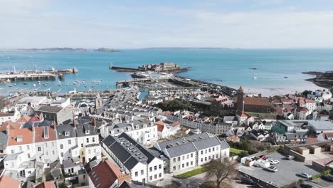 Flight-high-over-St-Peter-Port-roof-tops-out-to-sea-over-harbour,Albert-Marina,fishing-fleet-model-yacht-pond-and-Castle-Cornet-with-views-of-islands-on-sunny-day