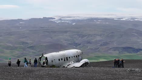 Drohnenaufnahme-Von-Touristen-Rund-Um-Ein-Flugzeugwrack-In-Der-Isländischen-Landschaft,-60 fps