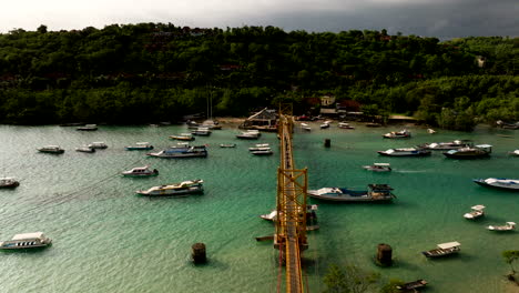 Berühmte-Gelbe-Brücke-In-Indonesien,-Die-Die-Inseln-Nusa-Lembongan-Und-Nusa-Ceningan-Auf-Bali-Verbindet,-Mit-Booten,-Die-Auf-Dem-Türkisfarbenen-Meerwasser-Schwimmen