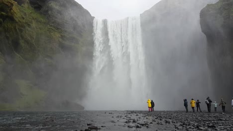 Turistas-Bajo-La-Cascada-De-Skogafoss-En-Un-Día-Lluvioso-De-Primavera,-Punto-De-Referencia-De-Islandia
