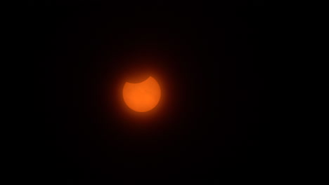 Partial-phase-of-a-solar-eclipse-resembling-a-jack-o-lantern-moves-across-a-hazy-sky