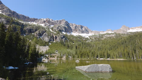 High-mountain-peak-above-an-alpine-lake-with-vast-forests