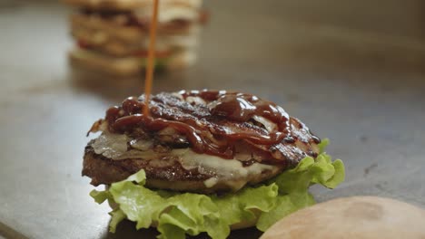 Pouring-tasty-savoury-sauce-on-succulent-grilled-burger,-fast-food-restaurant,