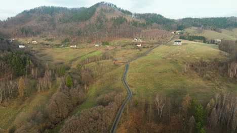 Eine-Kurvenreiche-Straße-Führt-Durch-Sanfte-Hügel-Und-Lichte-Wälder,-Mit-Einem-Hauch-Ländlicher-Besiedlung-Im-Hintergrund