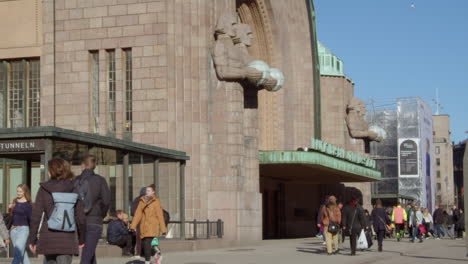 People-walk-past-brutalist-architecture-statues,-Helsinki-rail-station