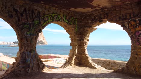 Peñon-d'Ifach---also-known-as-Calpe-Rock:-Dramatic-FPV-Drone-View-of-Calpe-Spains-Iconic-Mountain-and-Coastline-Through-Graffitied-Circular-Windows-in-an-abandoned-graffiti-building