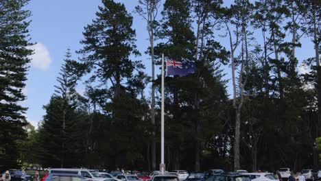 Neuseeland-Flagge-Weht-über-Einem-Grünen-Stadtpark,-Auf-Dem-Menschen-Spazieren-Gehen