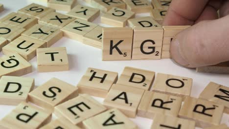 Hand-places-Scrabble-letter-tiles-on-table-forming-spy-acronym-KGB
