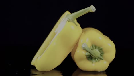 Gelbe-Paprika,-Vor-Einem-Schwarzen-Hintergrund,-Wobei-Eine-Hälfte-In-Scheiben-Geschnitten-Auf-Der-Anderen-Liegt,-Verkörpert-Das-Konzept-Kulinarischer-Kreativität-Und-Lebendiger-Frische
