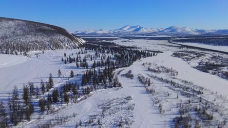 Río-Congelado-Con-El-Telón-De-Fondo-De-Montañas-Y-árboles-En-Yakutia-Desde-Un-Dron-De-4k