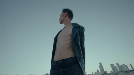 Young-caucasian-man-dances-on-roof-with-city-skyline-in-background