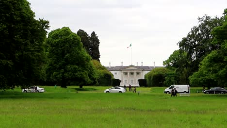 Fassade-Von-Aras-An-Uachtarain-Vom-Phoenix-Park-Aus-Gesehen,-Mit-Der-Irischen-Flagge-Im-Wind-Wehend