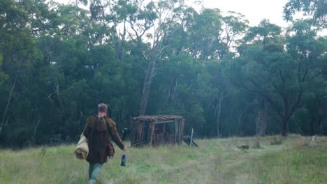 Un-Bosquimano-Caminando-Hacia-Una-Histórica-Cabaña-De-Corteza-En-El-Monte-Australiano.