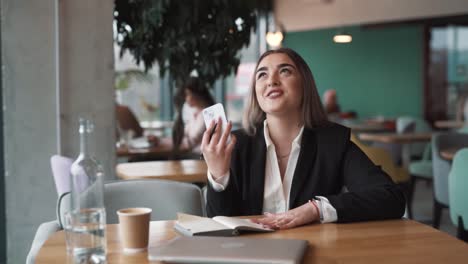 beautiful-woman-in-a-café,-wearing-business-attire,-receives-a-joyful-message-about-winning,-money,-and-victory