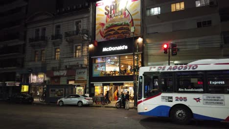 MC-Donald's-food-store-at-night-in-buenos-aires-city-avenue-bus-drive-by-nighttime-scene-cityscape-of-caballito-neighborhood-people-walk,-argentina