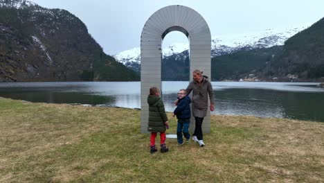 Tourists-having-fun-at-Portal-arch-statue-with-fjord-background,-rising-aerial