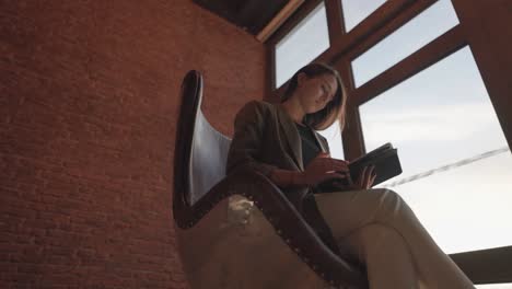 Low-angle-view-of-female-sit-on-leather-egg-chair-with-tablet-in-hands