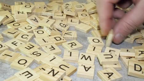 Right-hand-flips-Scrabble-tile-letters-over-on-table-top,-closeup-view