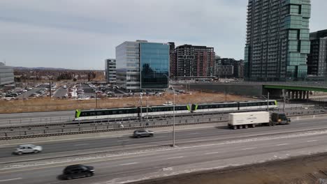 Das-Automatisierte-Stadtbahnsystem-Réseau-Express-Métropolitain-REM-In-Brossard,-In-Der-Nähe-Der-Stadt-Montreal,-Autobahnverkehr,-Autos-Und-Skyline-Auf-Einem-Modernen-Gebäude,-Quebec,-Kanada