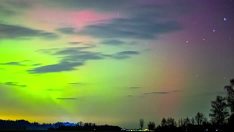 Aurora-Grüne-Lichter-Tanzen-über-Rosa-Nachthimmel-über-Wald,-Während-Wolken-Vorbeiziehen