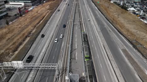 drone-following-Réseau-express-métropolitain-REM-automated-light-rail-system-in-Brossard,-near-Montreal-city,-on-the-main-road-highway-with-traffic-car,-Quebec-Canada