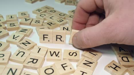 Right-hand-forms-word-FRAUD-from-scrabble-letter-tiles-on-white-table