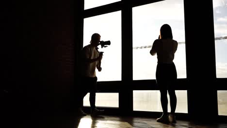 Female-model-near-bright-window-and-videographer-approach-with-camera