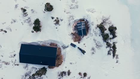 Above-View-Of-A-Cabin-Surrounded-By-Snow-In-Winter-Mountains