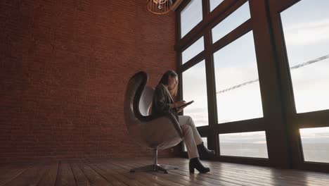 Frau-Sitzt-Auf-Einem-Retro-Leder-Eierstuhl-Mit-Aluminiumgehäuse-In-Der-Nähe-Des-Bürofensters