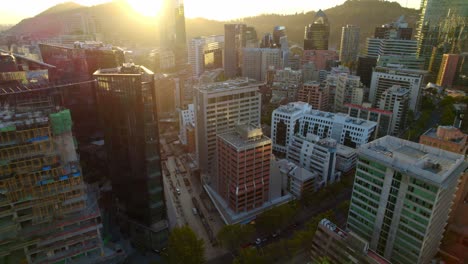 Aerial-tilt-shot-of-sunset-behind-vibrant-buildings-in-Las-Condes,-Santiago-de-Chile