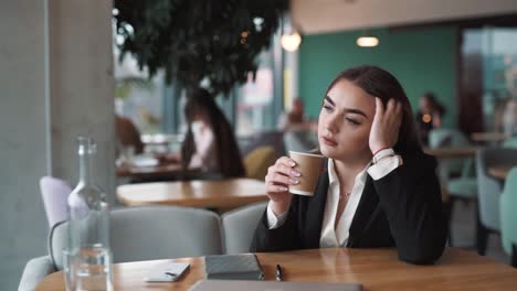 pensive,-beautiful-woman-sits-in-a-stylish-cafe-in-business-attire,-attentively-sipping-coffee