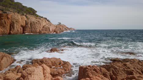 Ocean-waves-breaking-at-mediterranean-earthy-cliff-forest-in-Cami-de-Ronda-Spain-Costa-Brava,-rocky-landscape,-blue-sea-breaking