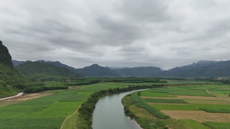 Luftaufnahme-Eines-Flusses,-Der-Durch-Getreidefelder-Fließt,-Mit-Regenwolken-Am-Himmel