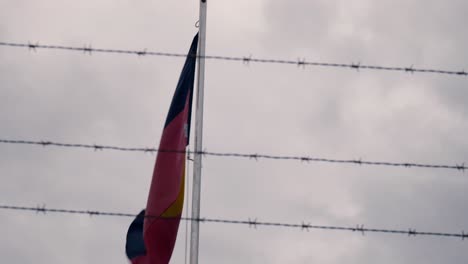 Australian-Aboriginal-flag-framed-by-barbed-wire-on-a-windy,-overcast-day