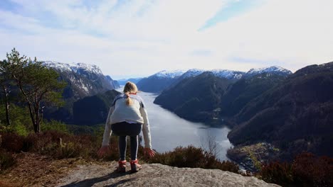 Young-woman-arrives-scenic-viewpoint-and-sit-down-to-enjoy-fjord-and-mountain-view,-Veafjord-Norway