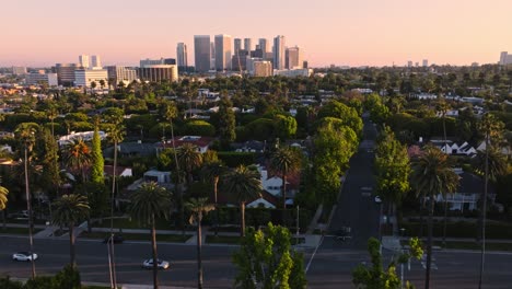 Aerial-Shot-of-Beverly-Hills-Intersection-with-Wilshire-Buildings-on-Horizon,-Cars-Driving-Along-Tree-Lined-Streets