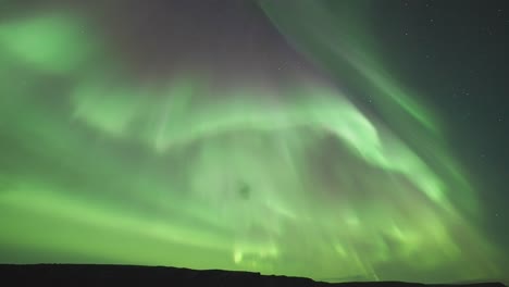 Ein-Zeitraffervideo,-Das-Die-Atemberaubende-Aurora-Borealis-Zeigt,-Wie-Sie-Sich-In-Einer-Dunklen-Winternacht-Anmutig-über-Einen-Ruhigen-Fjord-Bewegt.