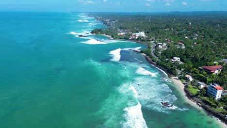 Aerial-drone-Indian-ocean-waves-crashing-into-bay-tropical-holidays-travel-town-landscape-along-coastline-Midigama-Weligama-Sri-Lanka-Asia-tourism